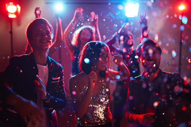 Group of friends celebrating at a lively party with confetti, dancing, and colorful lights