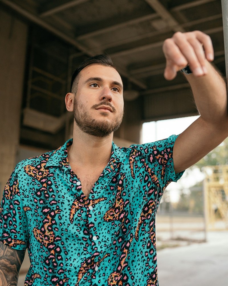 Man in patterned shirt reaching forward in industrial setting with blurred background.