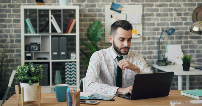 A male employee works on a laptop while sitting in an office