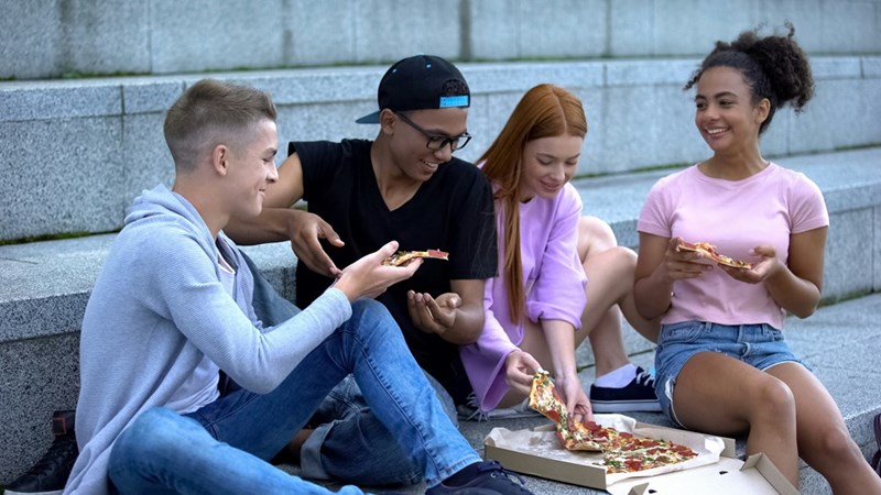 4 college kids snack on a pizza together while spending time outside.