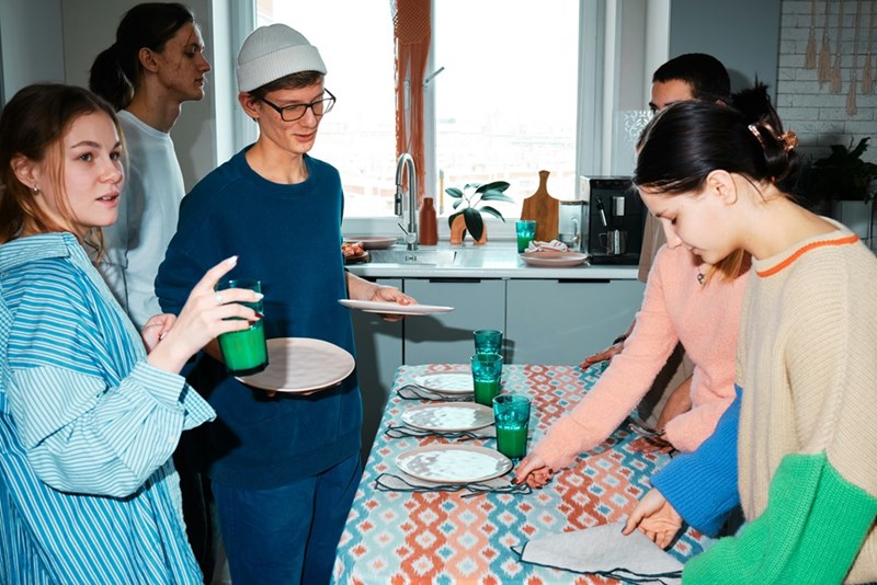 Group of college kids set the table before sharing a meal.