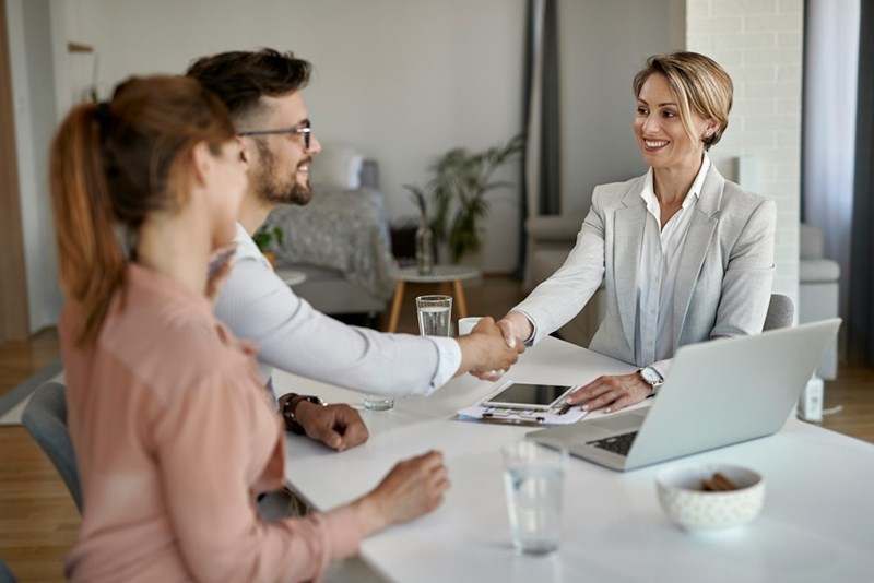 A man shakes hands with a bank manager across the table next to his partner.