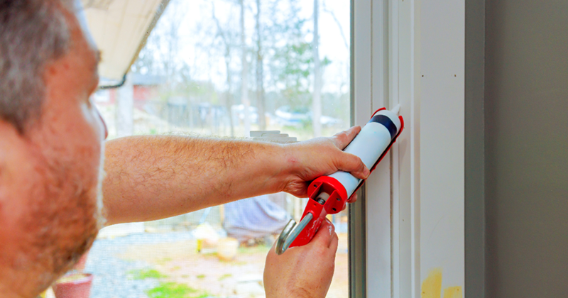 Homeowner applies caulking to seal window frame in residential area during works day