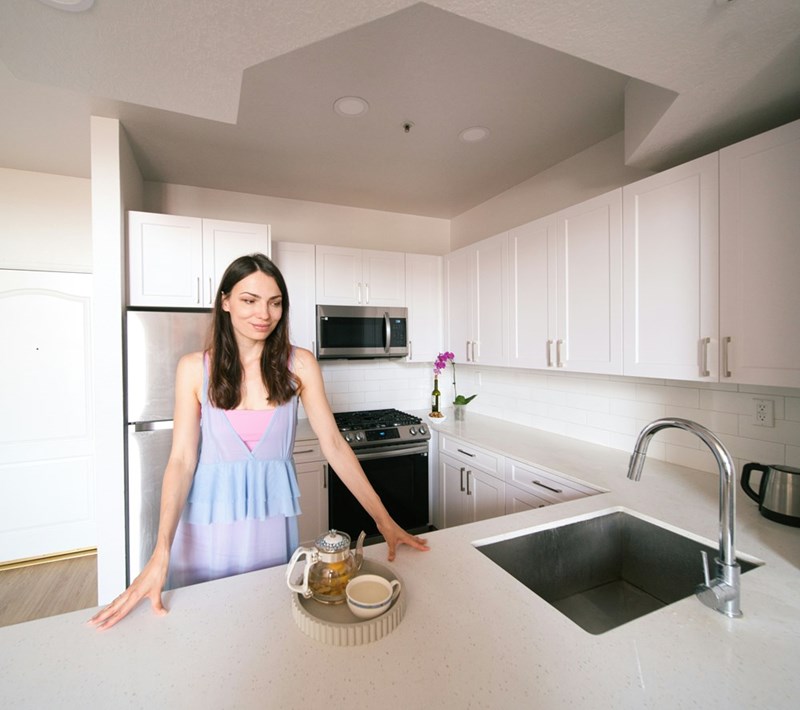 Woman standing at kitchen counter looking at tea set in bright modern kitchen interior.
