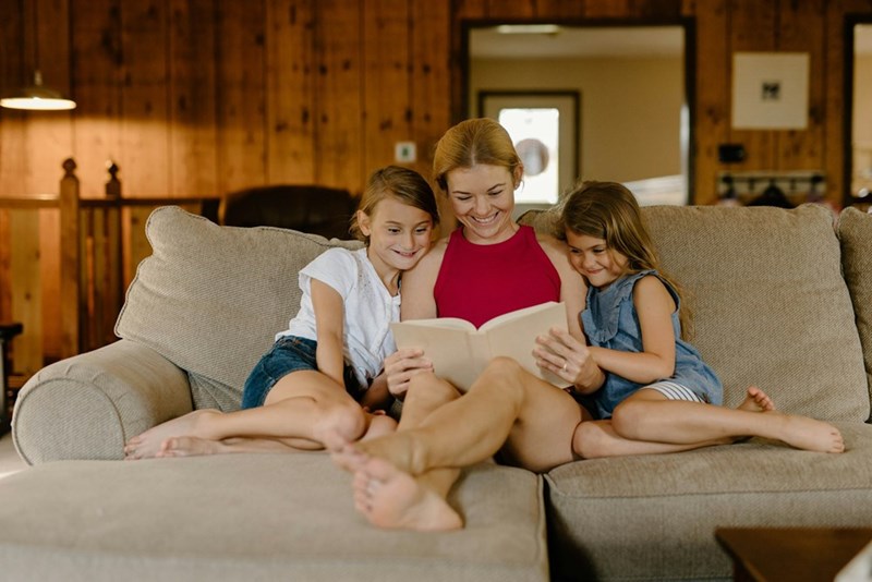 Mother reading book with two children on sofa in cozy living room