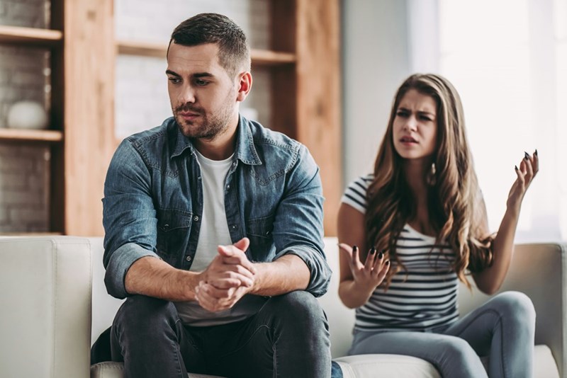 Angry couple dressed casually sitting down in a couch arguing.
