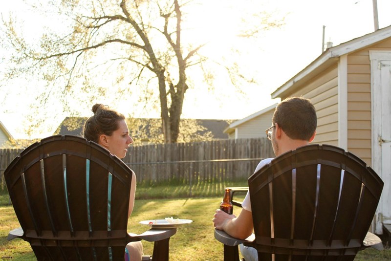 Two people sitting in a chair in the backyard talking.