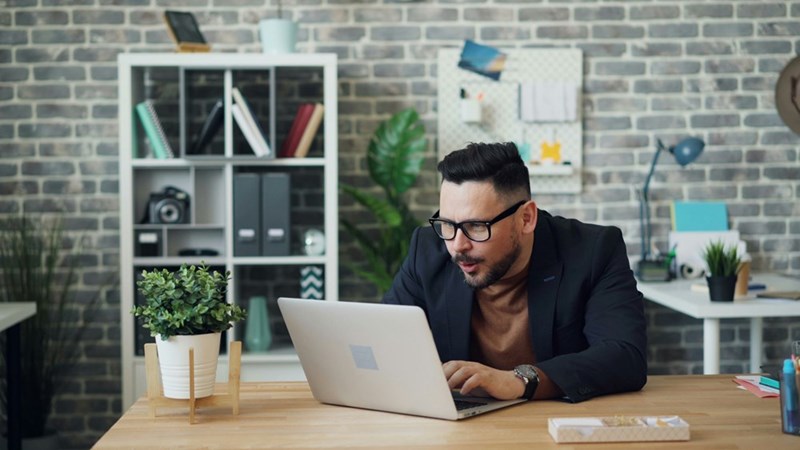 A male coworker expresses excitement as he looks closely at something on his computer.