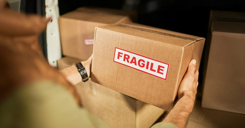 Male delivery driver takes a box out of the back of his van labelled 'fragile'
