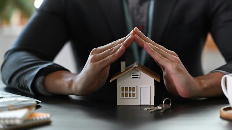 A landlord carefully holds his hands over a model house in symbolic nature
