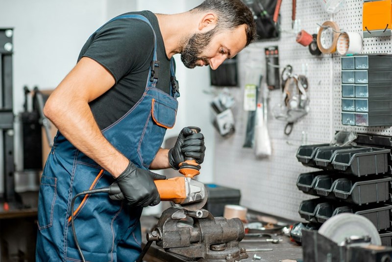 A car-savvy mechanic uses a power grinder in a workshop while repairing automotive parts