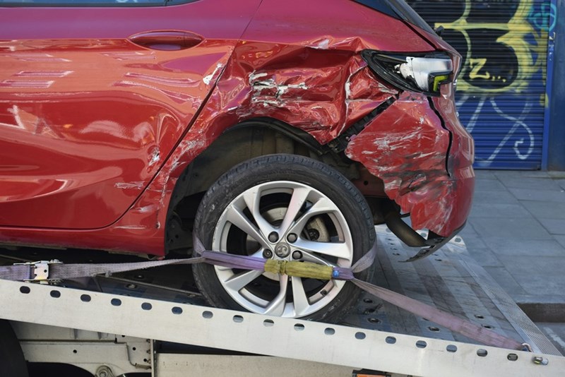 Damaged red car with severe rear-end collision sits on a tow truck after an accident