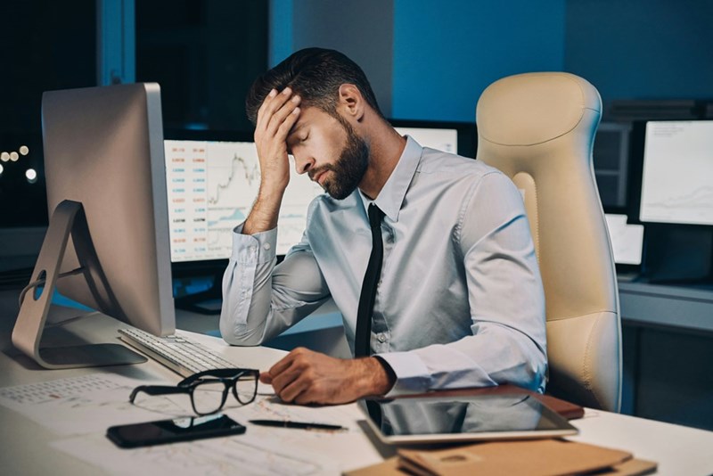 Frustrated young man in shirt and tie holding his head while staying late in the office