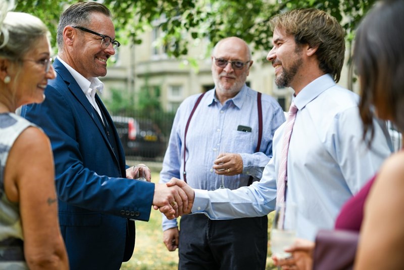 A group of people is standing outside dressed formally smiling and shaking hands.