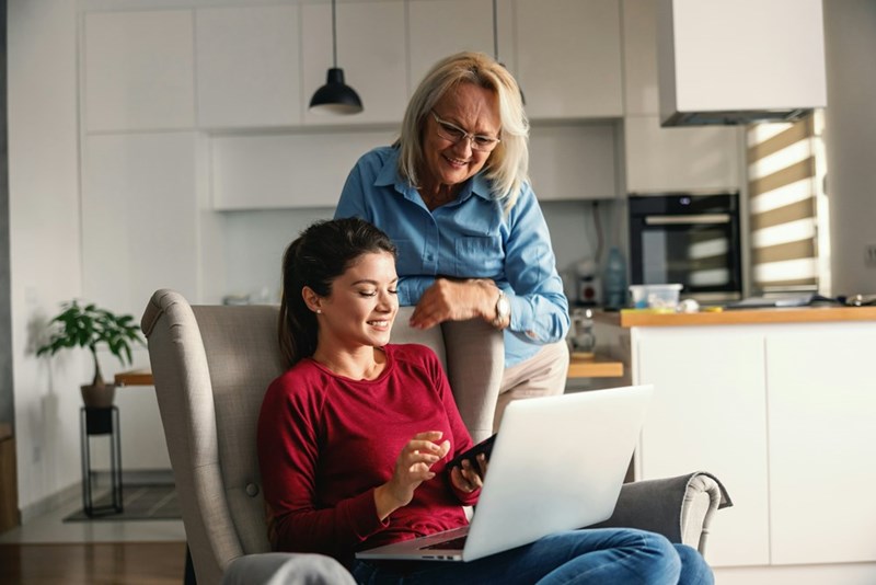 An elder woman and a younger woman look at a computer and smile.