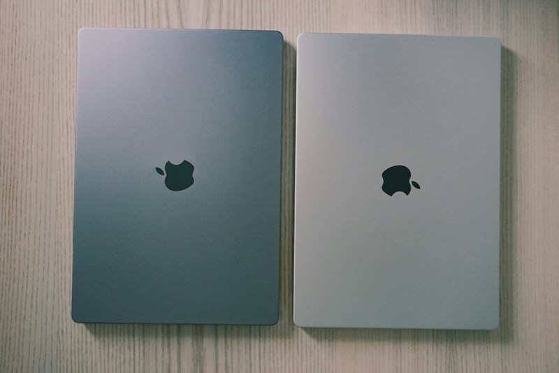 Two MacBooks computers of different grey tone colors places on a wood surface.