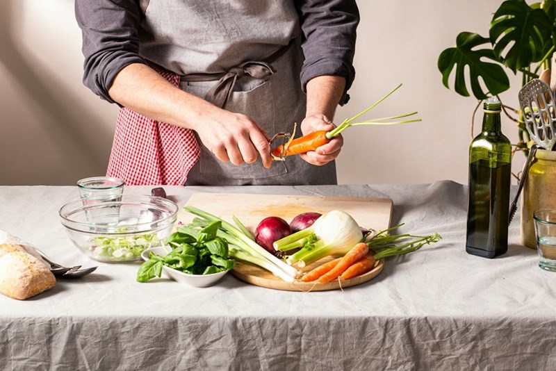 A home cook peels fresh vegetables on a kitchen counter, highlighting healthy cooking, meal prep, and homemade food preparation.