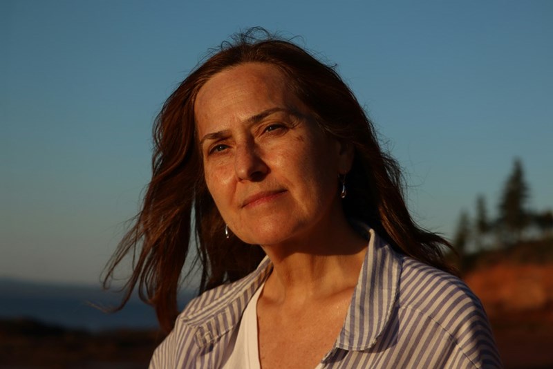 Woman in sunset light outdoors with windblown hair, looking at camera with a contemplative expression.