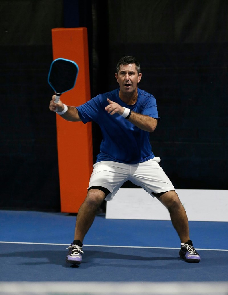 Man in ready position with paddle on indoor pickleball court preparing for return.
