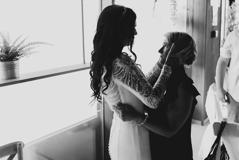 Bride wearing dress and holding upset mother's face.