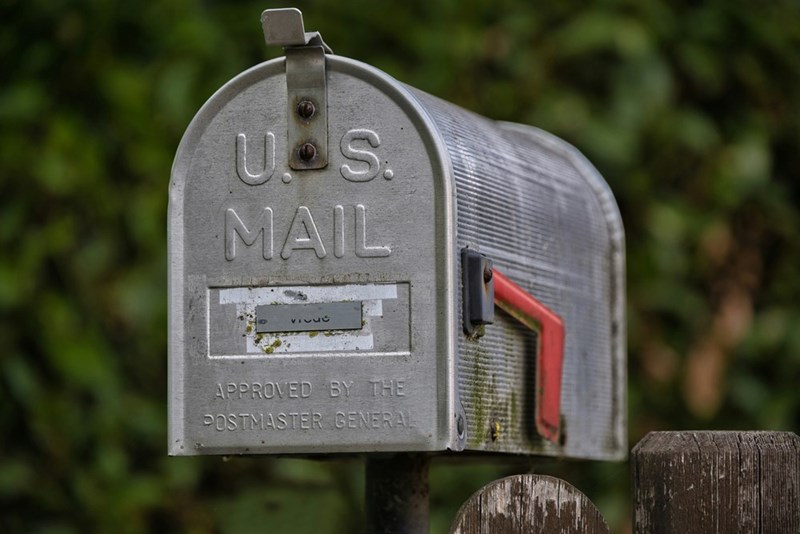 Classic silver metal US mailbox, standing on a wooden post in a residential area.