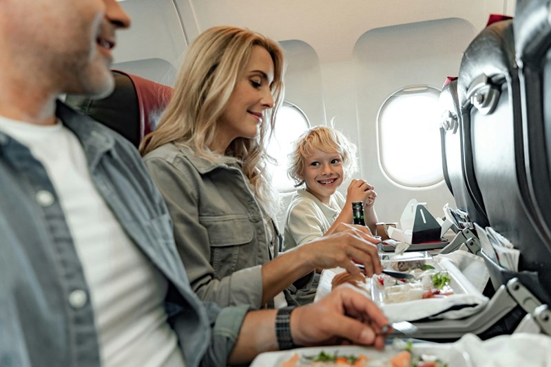 Grinning little boy sits next to his peaceful-looking Mom and Dad on a flight.