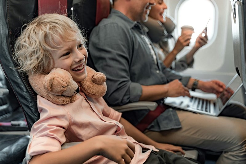 Little boy laughs while sitting next to his distracted parents on a plane.
