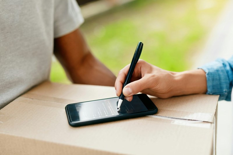 Woman's hand signing an electronic delivery receipt on a mobile app for a received package.
