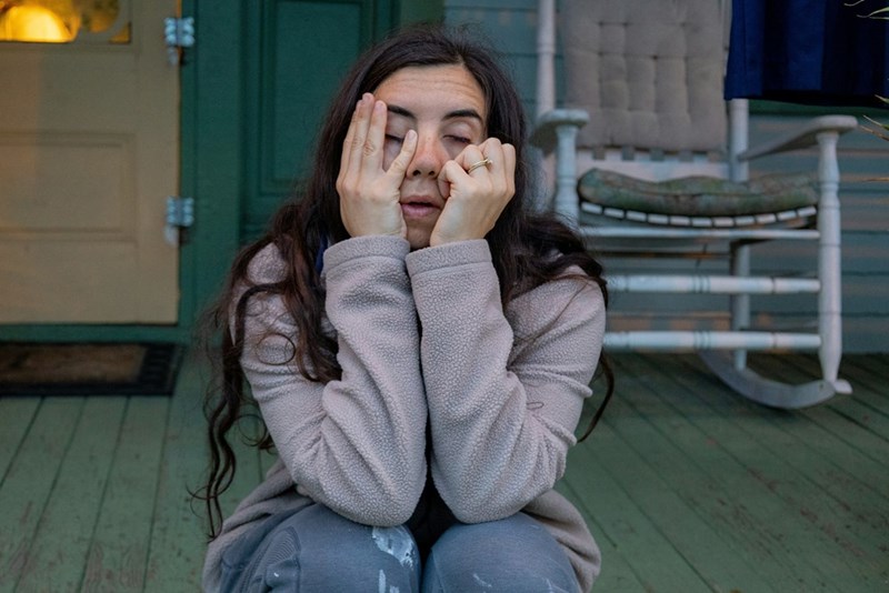 A woman sits on a porch looking exhausted