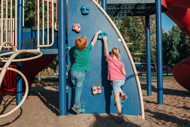 Little preschool boy and girl climbing rock wall at playground outside on summer day