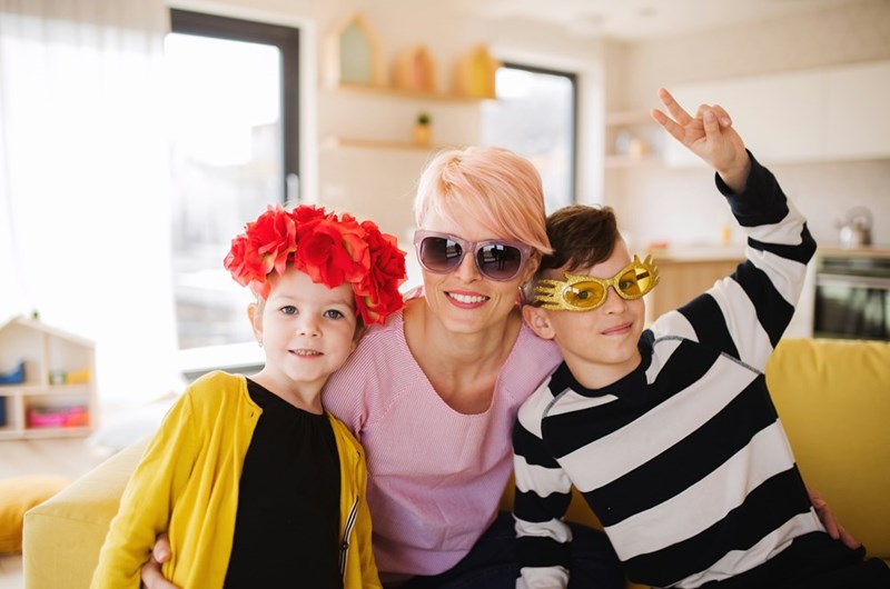 Short-haired woman with glasses smiling to the camera with two kids wearing party accessories