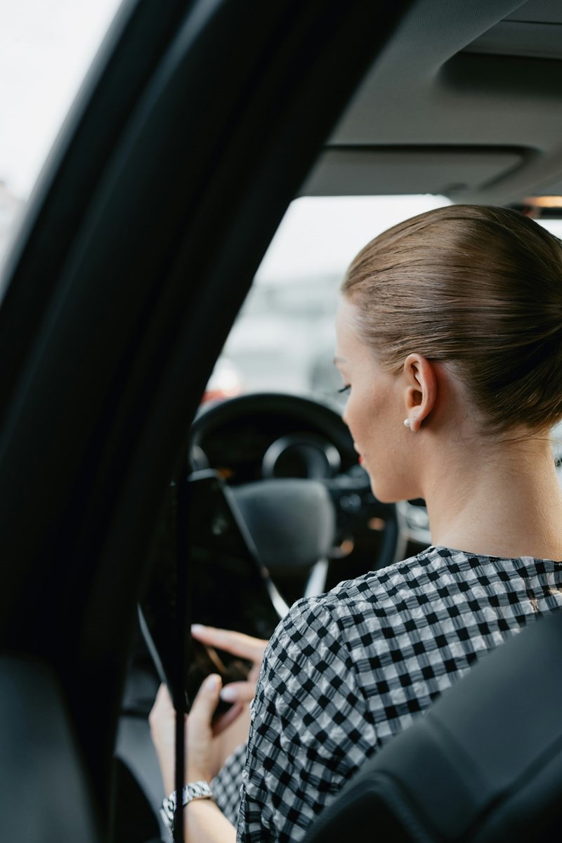 Woman reading a text message on her phone while sitting on the car.