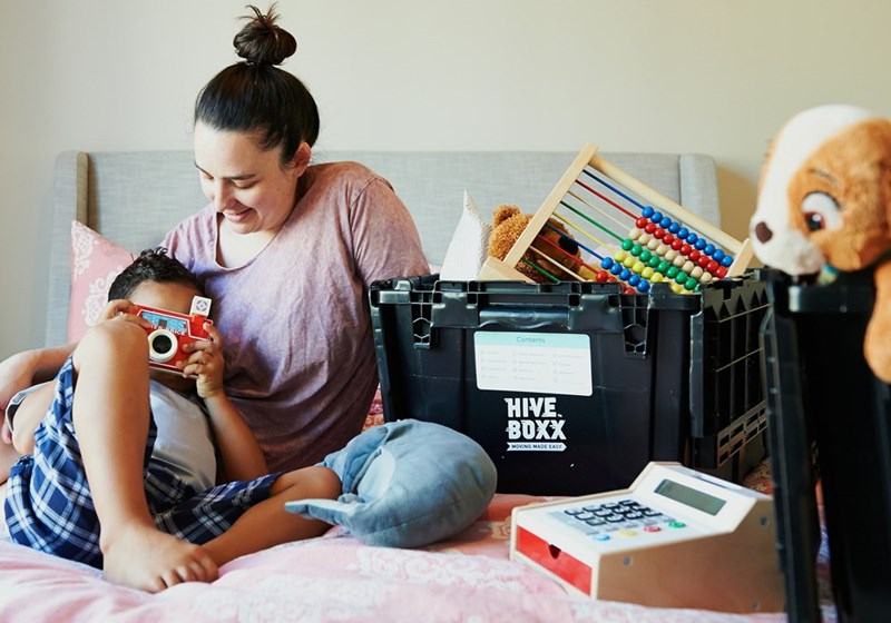 A mother and child laying down on a bed with a black box filled with instruments besides them.