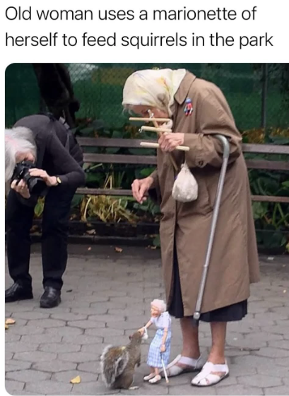 Old woman uses a marionette of herself to feed squirrels in the park