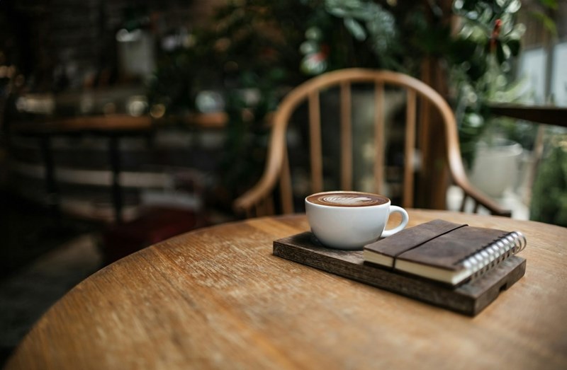 Cup of coffee and notebook on a wooden table in a cafe, representing a relaxing workspace, productivity, and minimalist lifestyle aesthetic