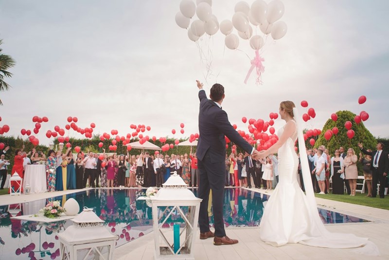Outdoor wedding celebration with bride and groom releasing balloons surrounded by guests, capturing a joyful ceremony moment and romantic event atmosphere