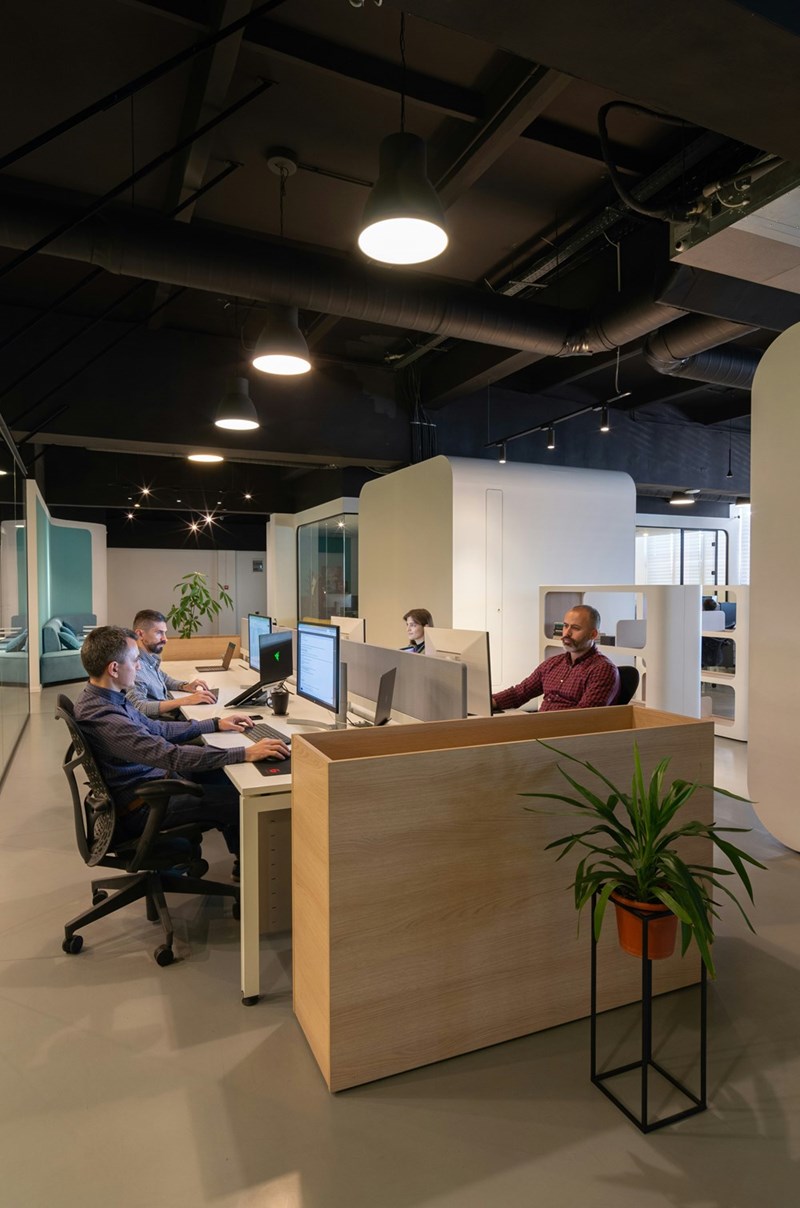 Team working at computers in modern open-plan office with desks, partitions, and overhead lighting.