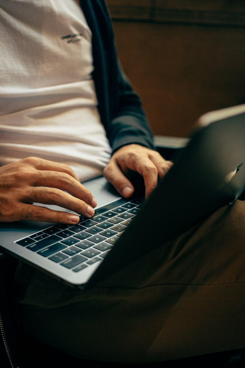 Man hands typing on a laptop computer sitting on his lap