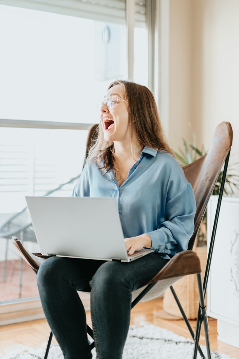 Woman sitting on a folding chair with a laptop computer in her lap, laughing at someone unseen