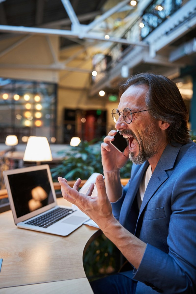 Older man, angry, looking at his laptop computer, screaming on the phone