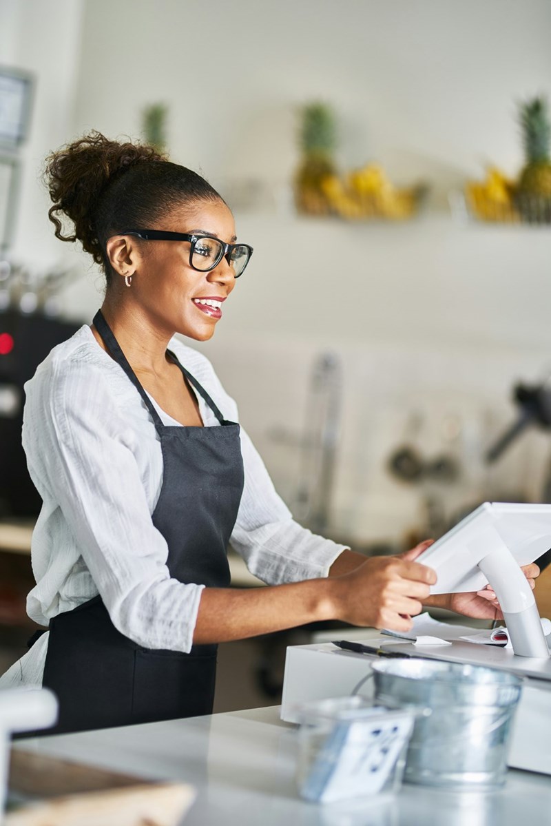 Friendly shop assistant using POS terminal to input orders at restaurant during the day