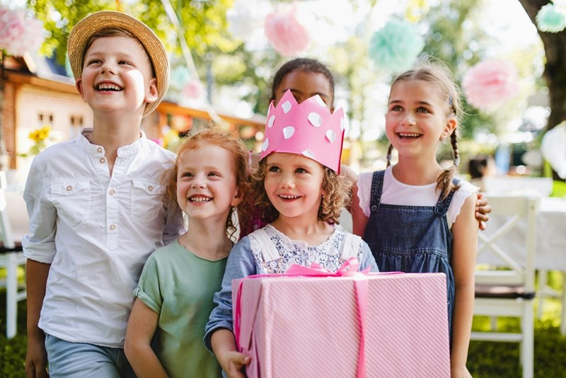Little girl and her friends celebrate a birthday party while she holds a huge present.
