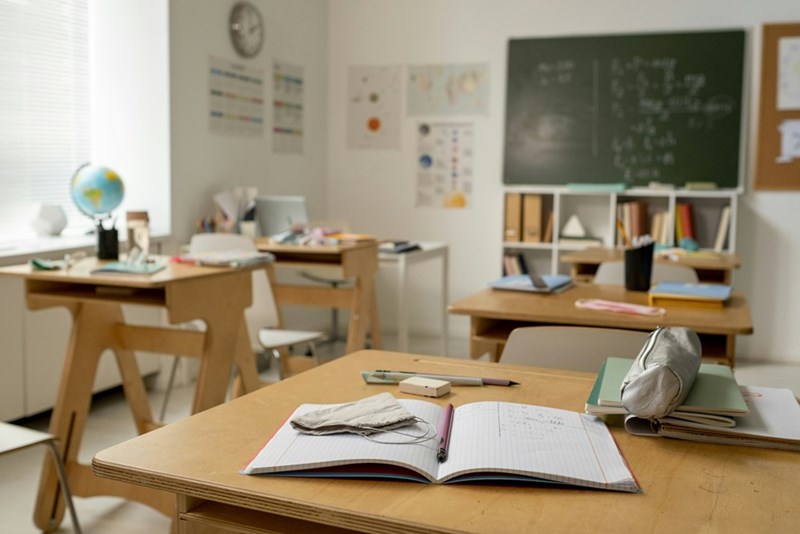 A student's desk in a high school classroom with an open notebook on top.