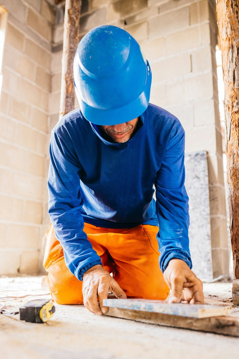A man in a blue hardhat is working on constructing flooring