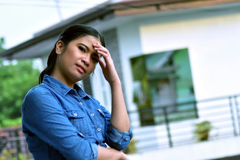 A frustrated homeowner leans her head against her left hand as she stands outside her house.