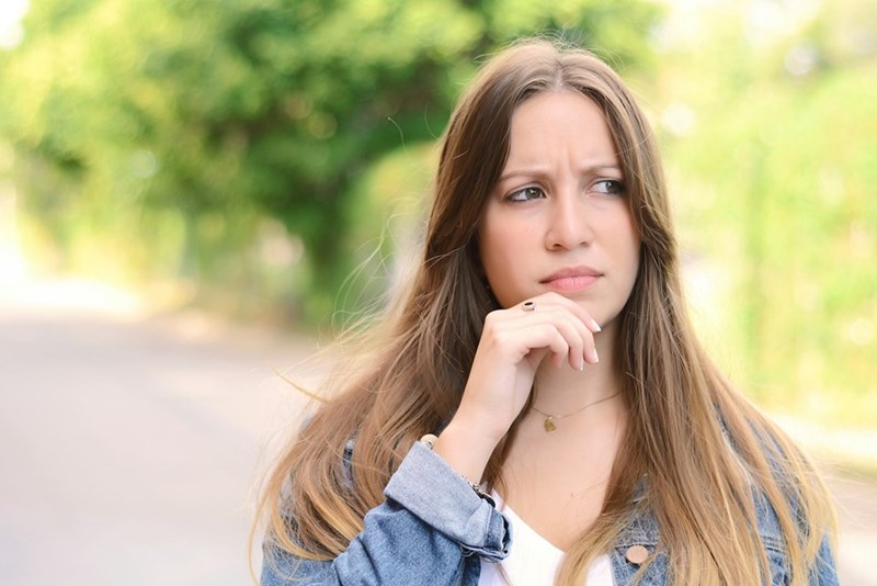 Young woman thinking outdoors in park, close-up portrait with natural light and thoughtful expression