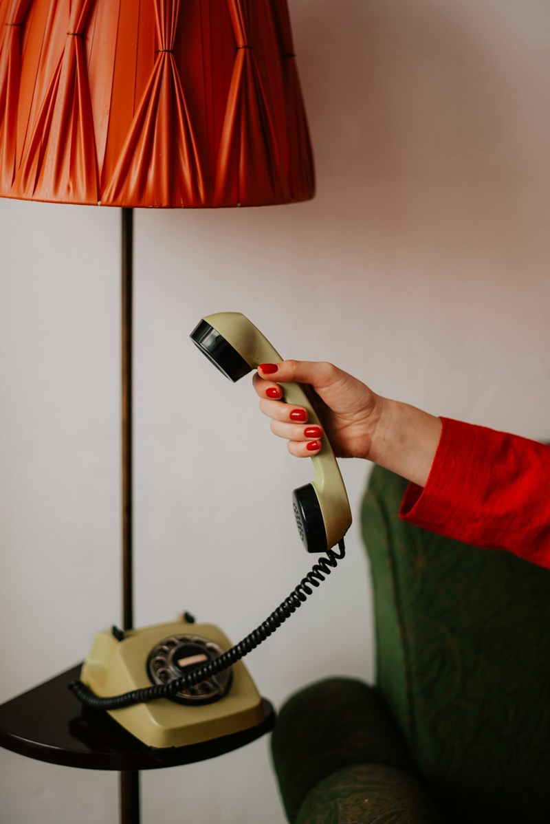 A woman picks up an old-fashioned phone by the bedside table.