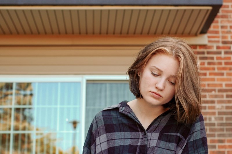 The frustrated homeowner looks upset while sitting in front of the entrance to her home.