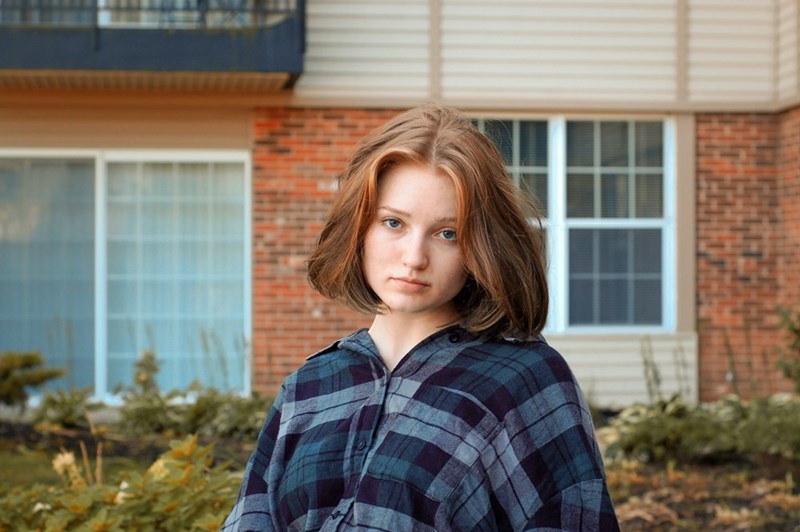 The frustrated homeowner looks upset while standing in front of the entrance to her home.