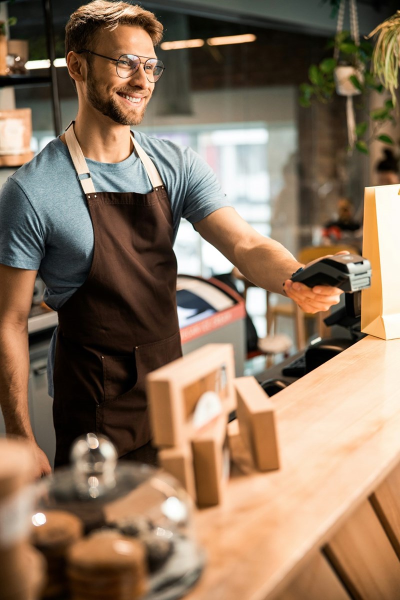 Barista holds out cashless device for customer to pay for beverage.